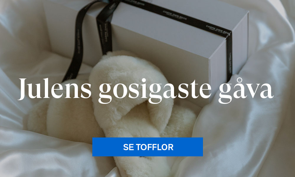 Vita tofflor på silkessängkläder med ett inslaget paket i bakgrunden.